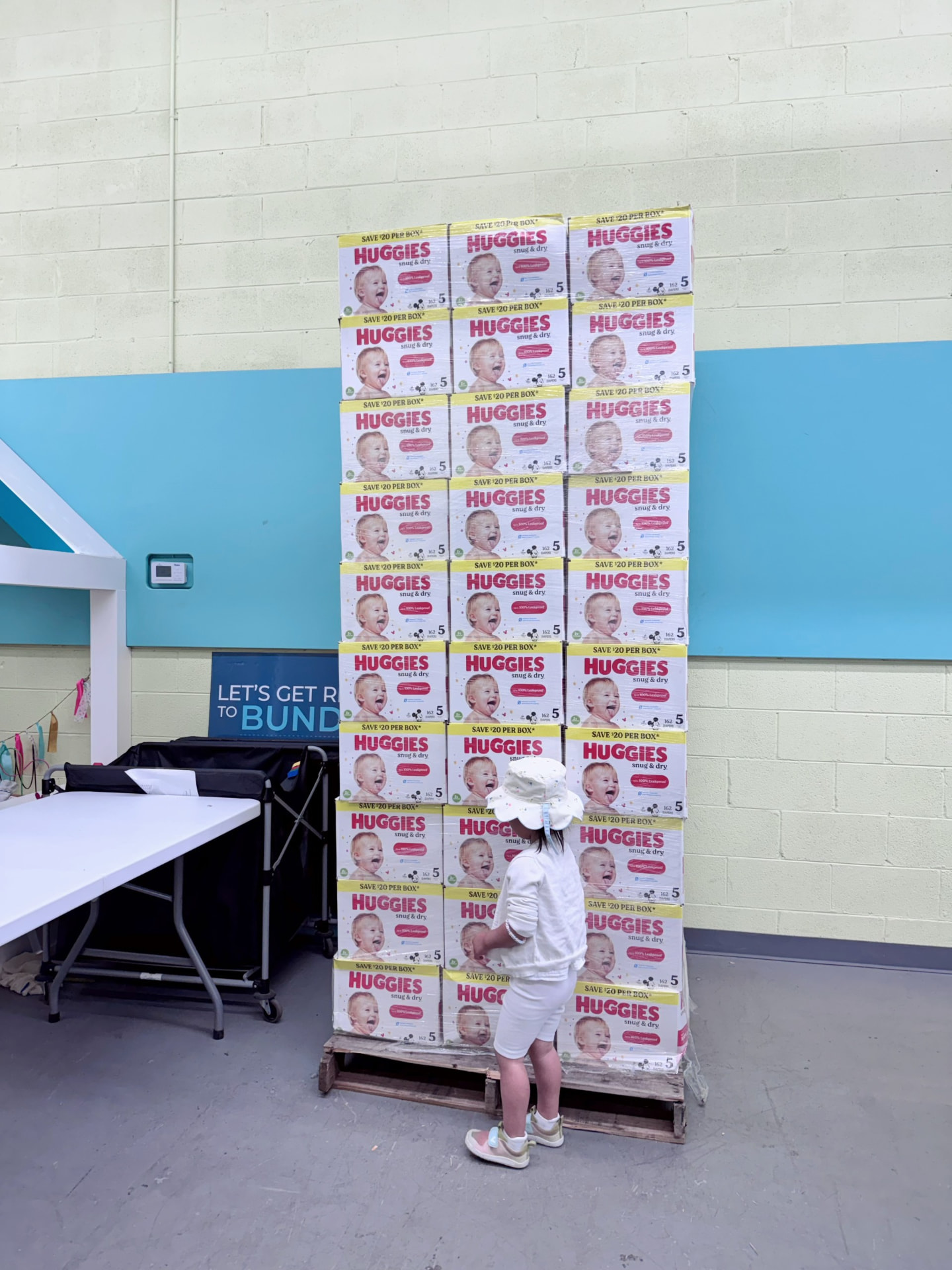 Amanda Lee Liu’s daughter standing beside a tall stack of donated diaper boxes at a diaper bank.